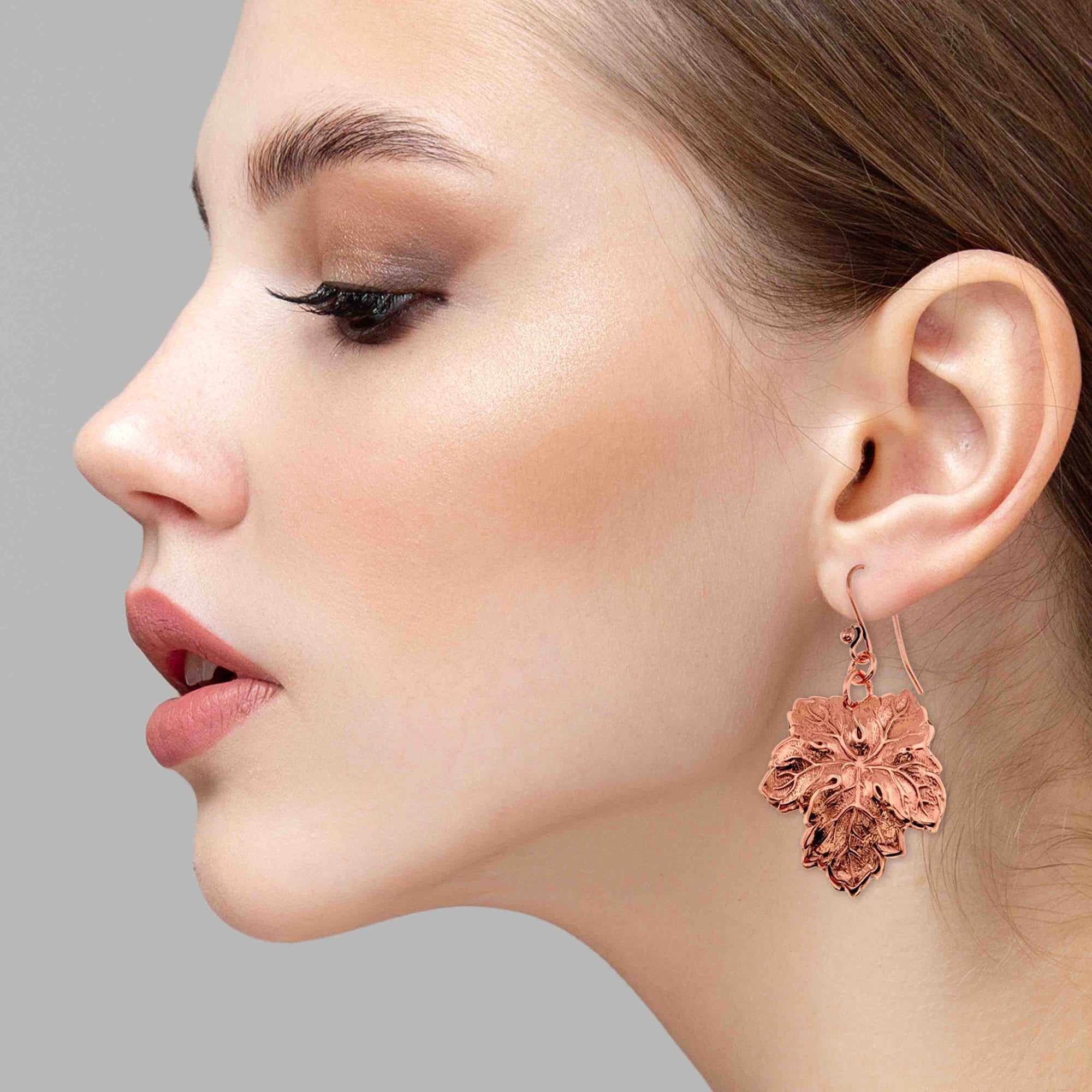 Close-up of a woman wearing Grape Leaf Copper Dangle Earrings against a gray background