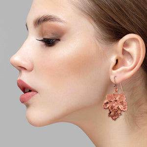 2 of 6: Close-up of a woman wearing Grape Leaf Copper Dangle Earrings against a gray background