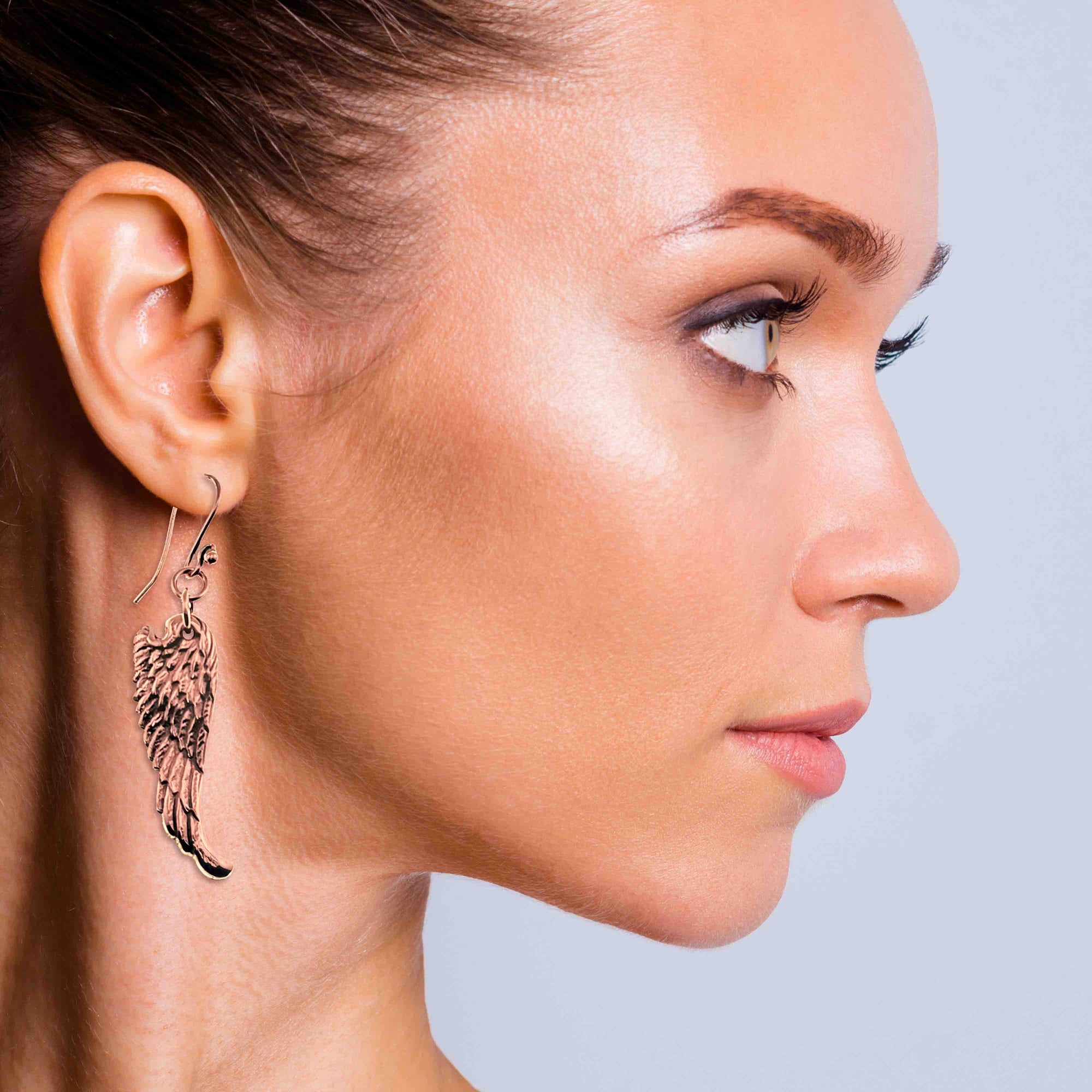 Close-up of a woman wearing Copper Guardian Angel Wing Drop Earrings against a neutral background