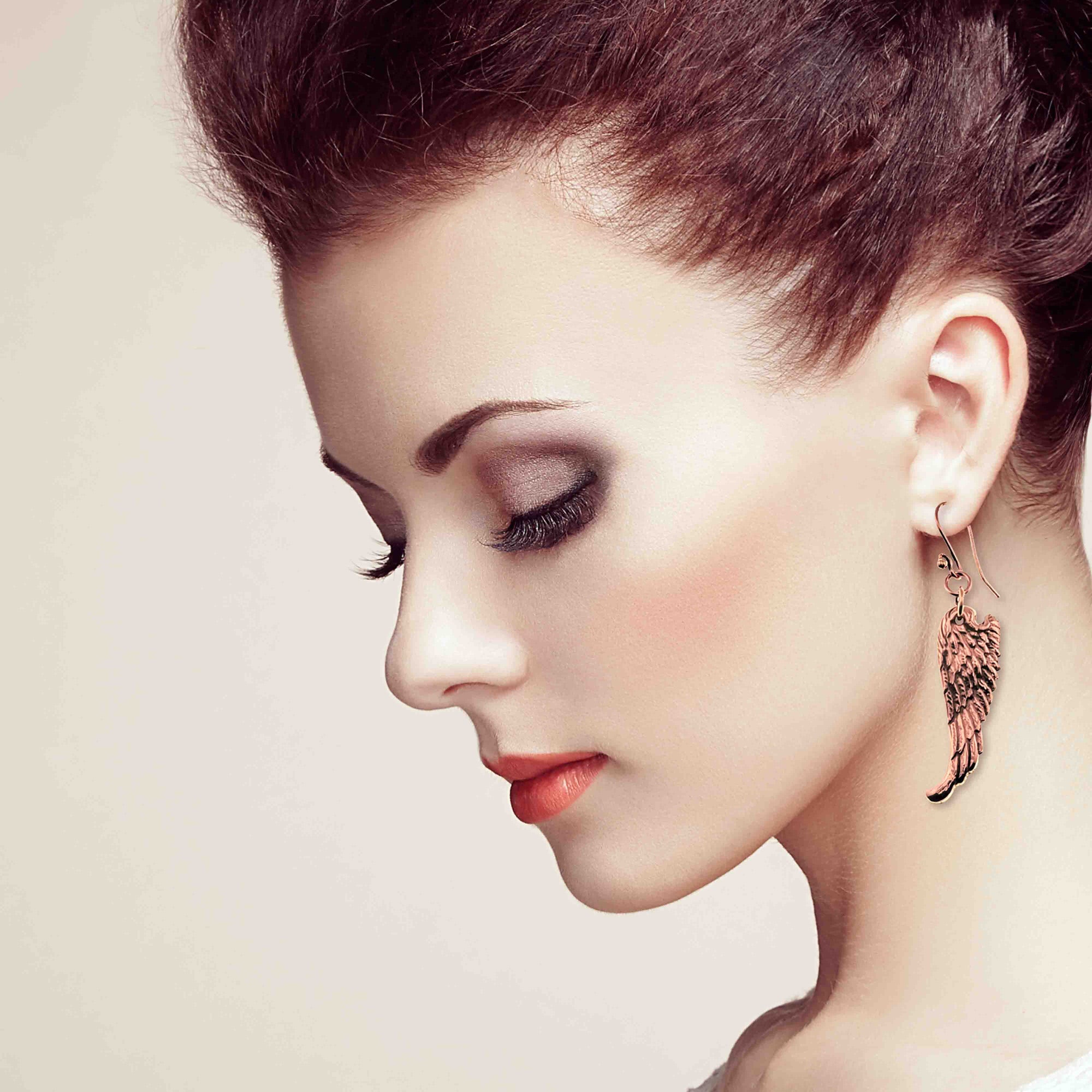 Close-up of a woman's profile with a focus on her Copper Guardian Angel Wing Drop Earrings against a neutral background