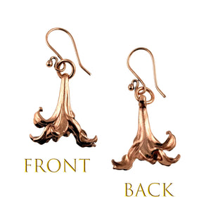 3 of 7: A side-by-side image showing the front and back views of a pair of handcrafted copper lily flower drop earrings. The front view displays detailed die-struck petals with textured grooves, while the back view reveals a smoother, slightly rounded finish. Both earrings hang from copper French ear wires. Text labels "FRONT" and "BACK" in gold font indicate each view.