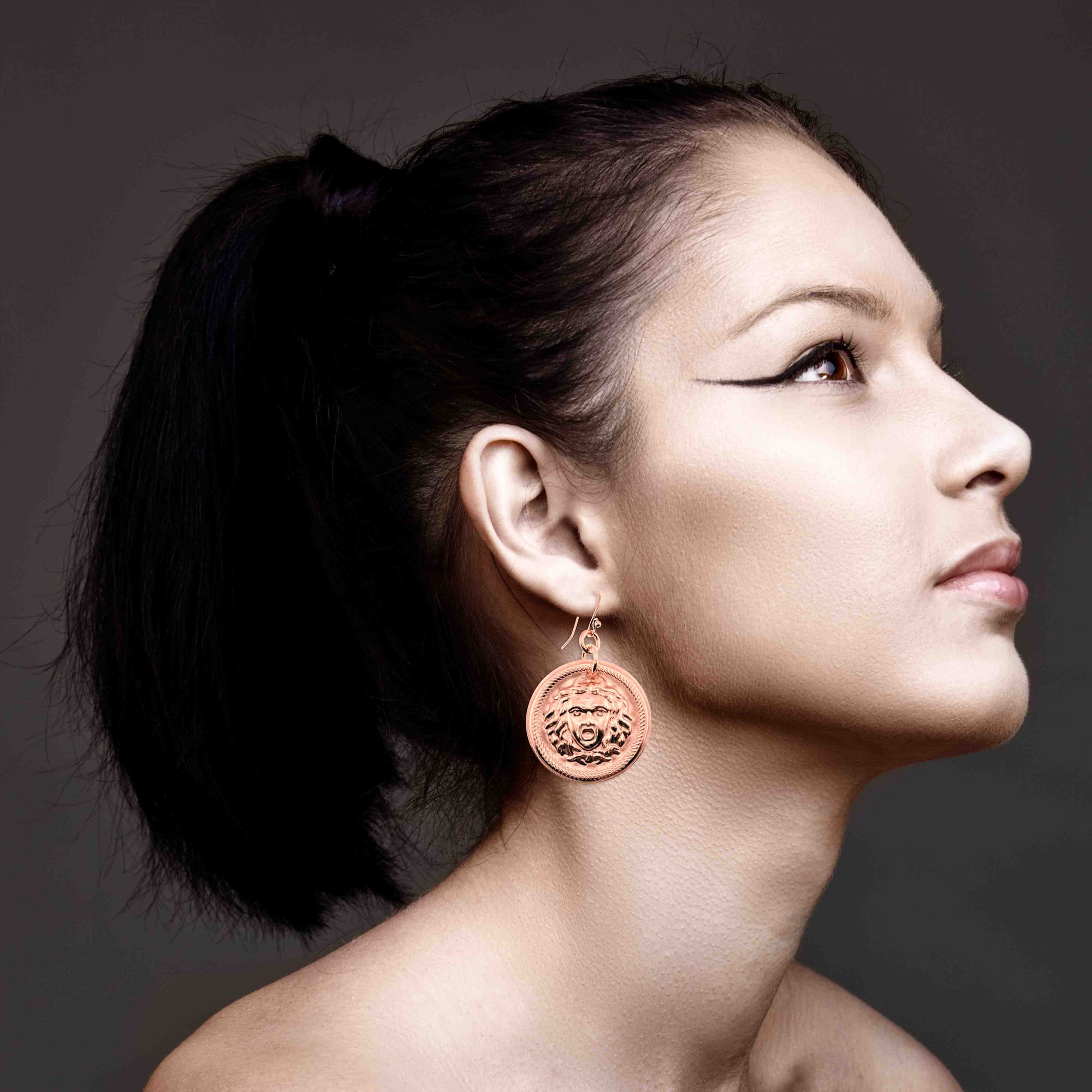 Woman wearing Copper Medusa Disc Drop Earrings against a dark background