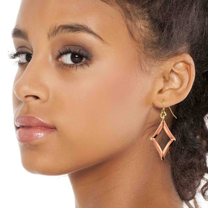 4 of 7: Close up portrait of a woman with dark curly hair pulled back, wearing a handcrafted copper open diamond drop earring. The polished geometric copper frame hangs from a brass French ear wire, adding a warm metallic accent against her smooth skin and neutral makeup. The open diamond shape dangles just below her earlobe, highlighting the modern minimalist design.