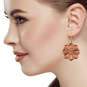 4 of 7: Close up side profile of a woman wearing a polished copper flower dangle earring. The eight petal bloom features raised, die struck detailing and a warm rosy copper shine. The earring hangs about 2 inches below the earlobe from a brass French hook ear wire. The image shows scale, movement, and how the floral design frames the face against a light background.