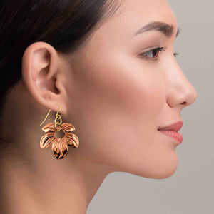2 of 7: Side profile of a woman wearing a handcrafted copper petal blossom dangle earring with polished floral detailing and an open center, hanging from a brass French ear wire against a soft neutral background.