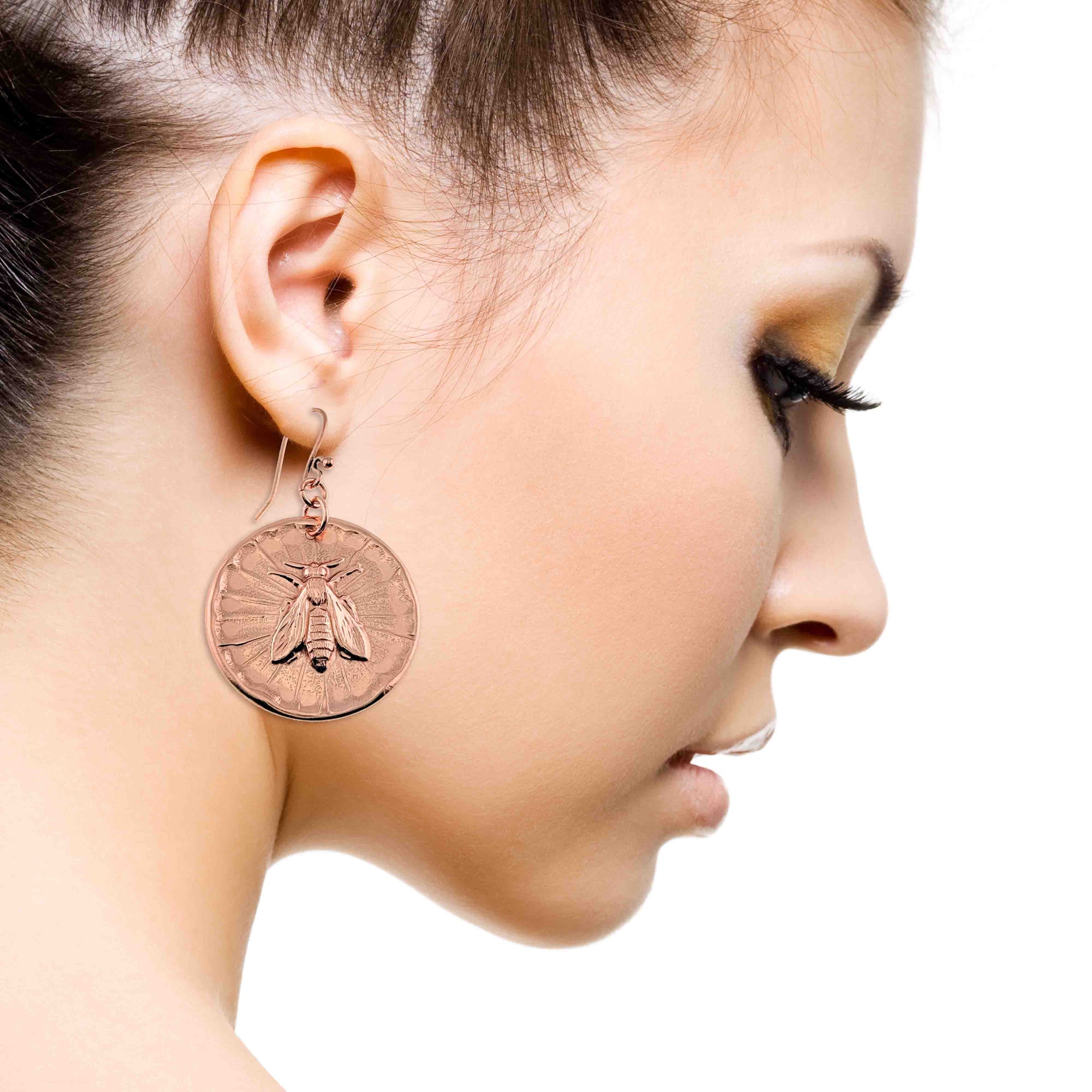 Close-up of a woman wearing a large round earring with a bee design on a white background