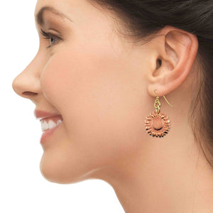 4 of 7: Side profile of a smiling woman wearing copper sunflower dangle earrings with detailed petals and a textured center. The warm copper charm hangs from a gold tone brass French hook, adding a soft, natural glow. Set against a clean light background, the earring offers a feminine floral accent suited for everyday wear or seasonal styling.