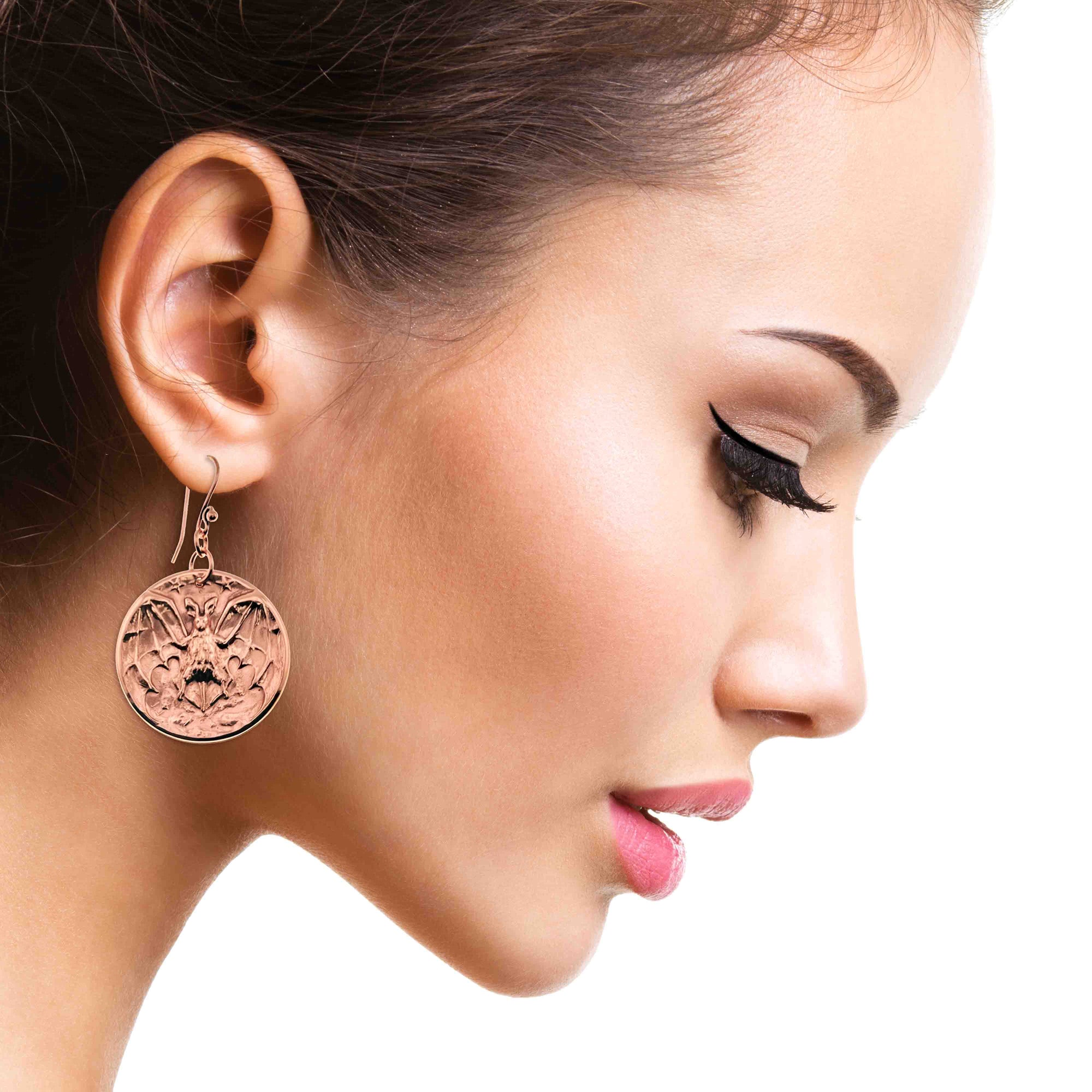 Close-up of a woman wearing Copper Vampire Bat Disc Dangle Earrings on a white background