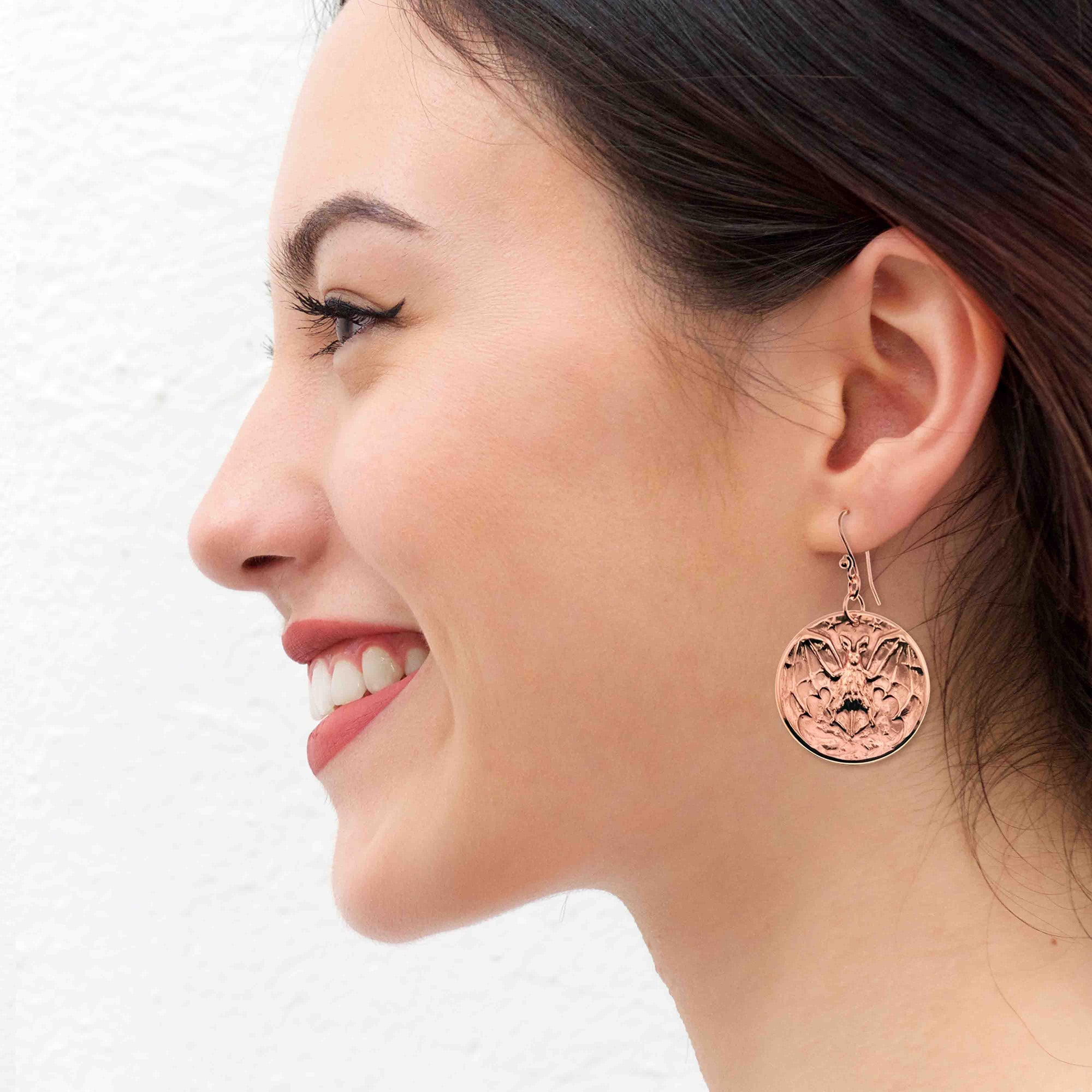 A Smiling woman wearing Copper Vampire Bat Disc Dangle Earrings with a white background