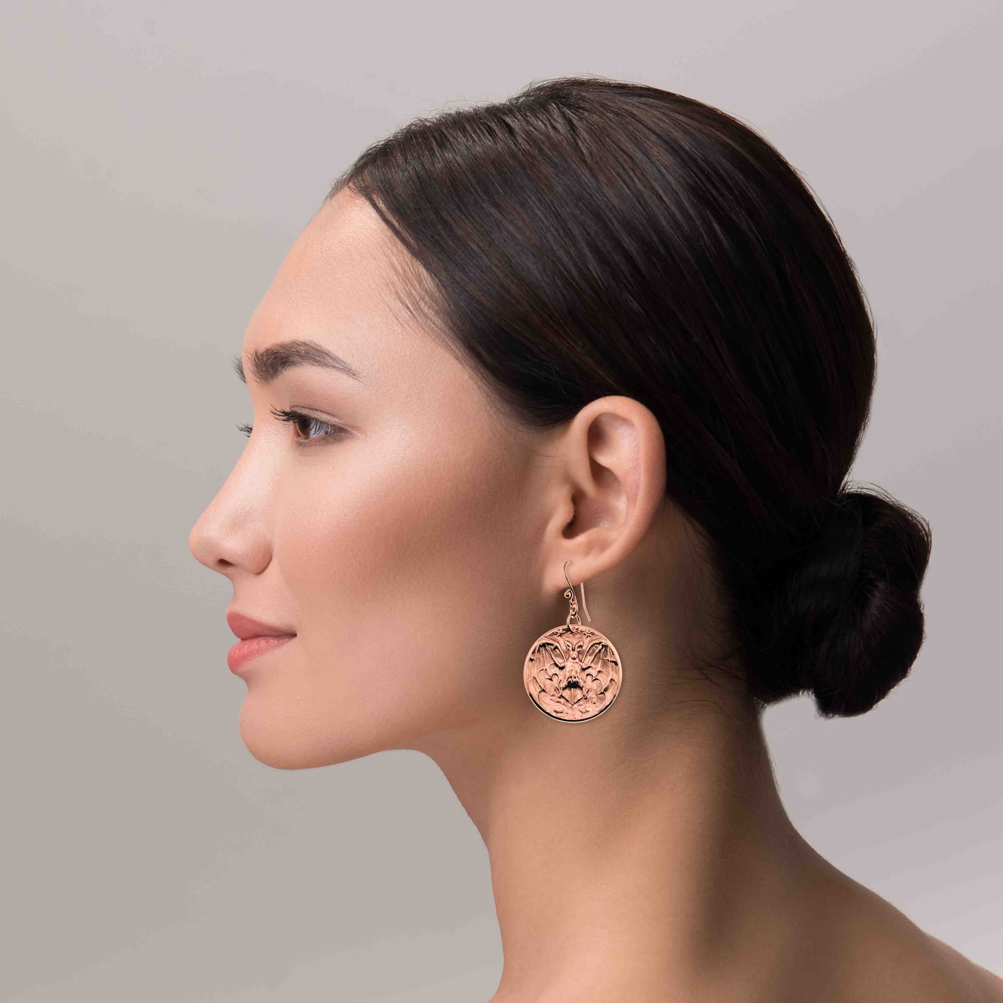 Woman wearing Copper Vampire Bat Disc Dangle Earrings with a plain background