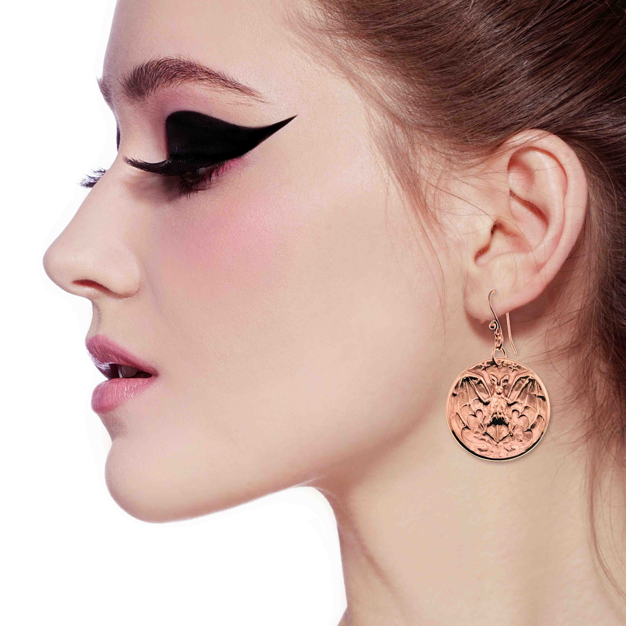 Close-up of a woman's profile wearing Copper Vampire Bat Disc Dangle Earrings with a white background