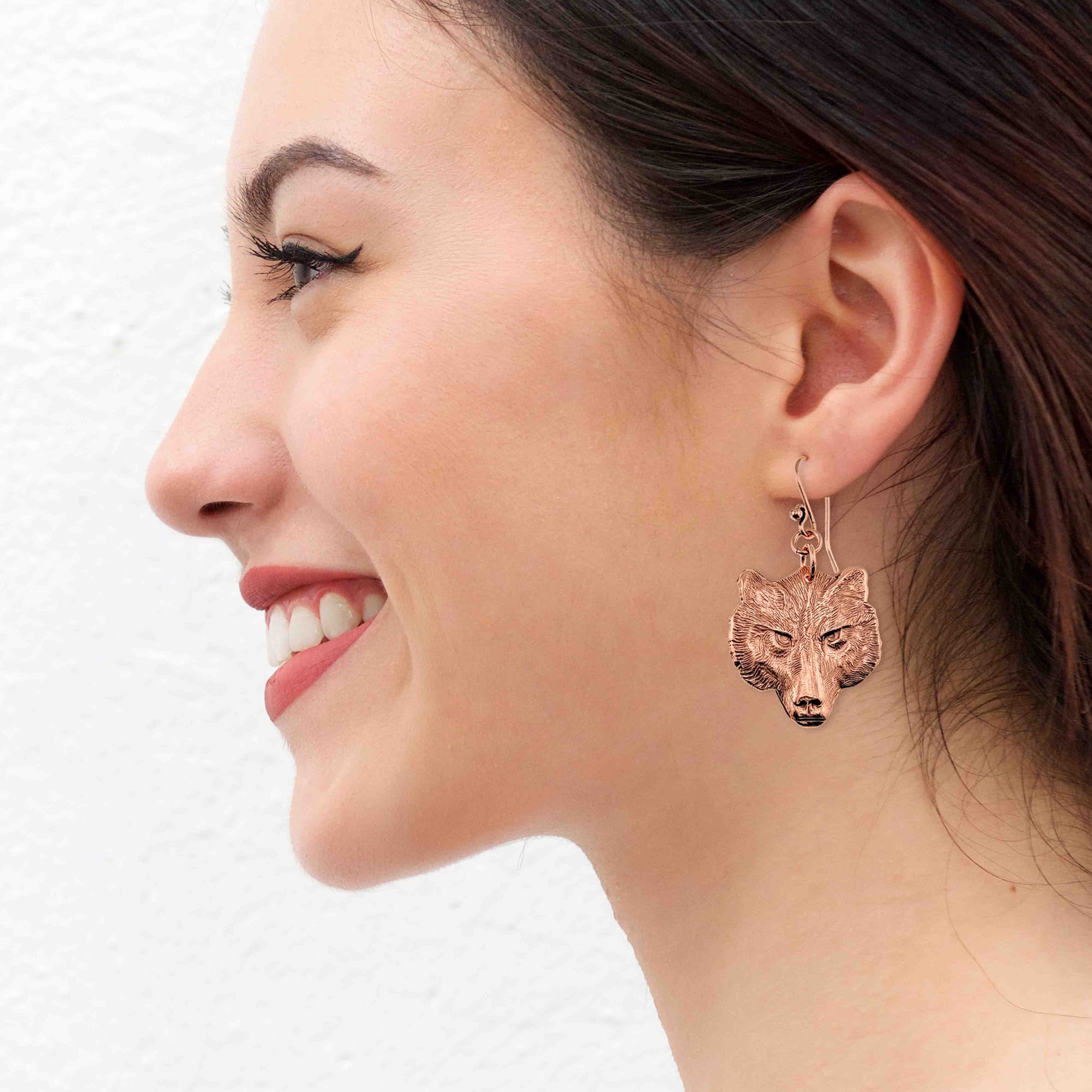 Close-up of a woman wearing a copper wolf-shaped earring on a white background