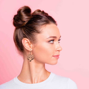 4 of 7: Woman with styled hair and Wolf Head Copper Drop Earrings against a pink background