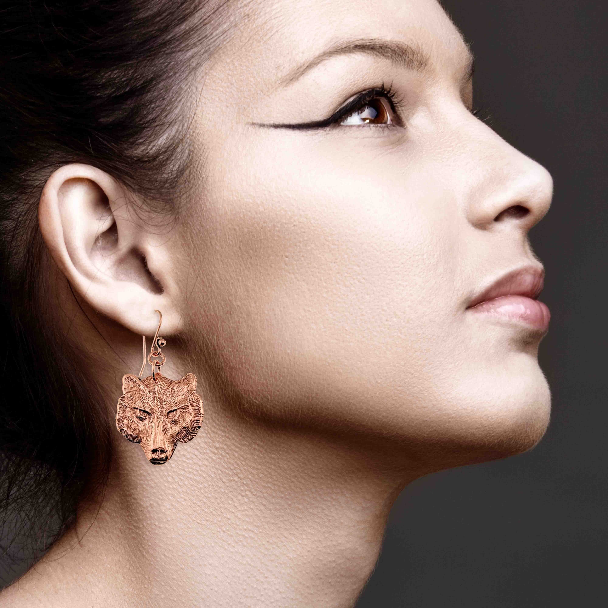 Close-up of a woman wearing a wolf-shaped earring against a dark background