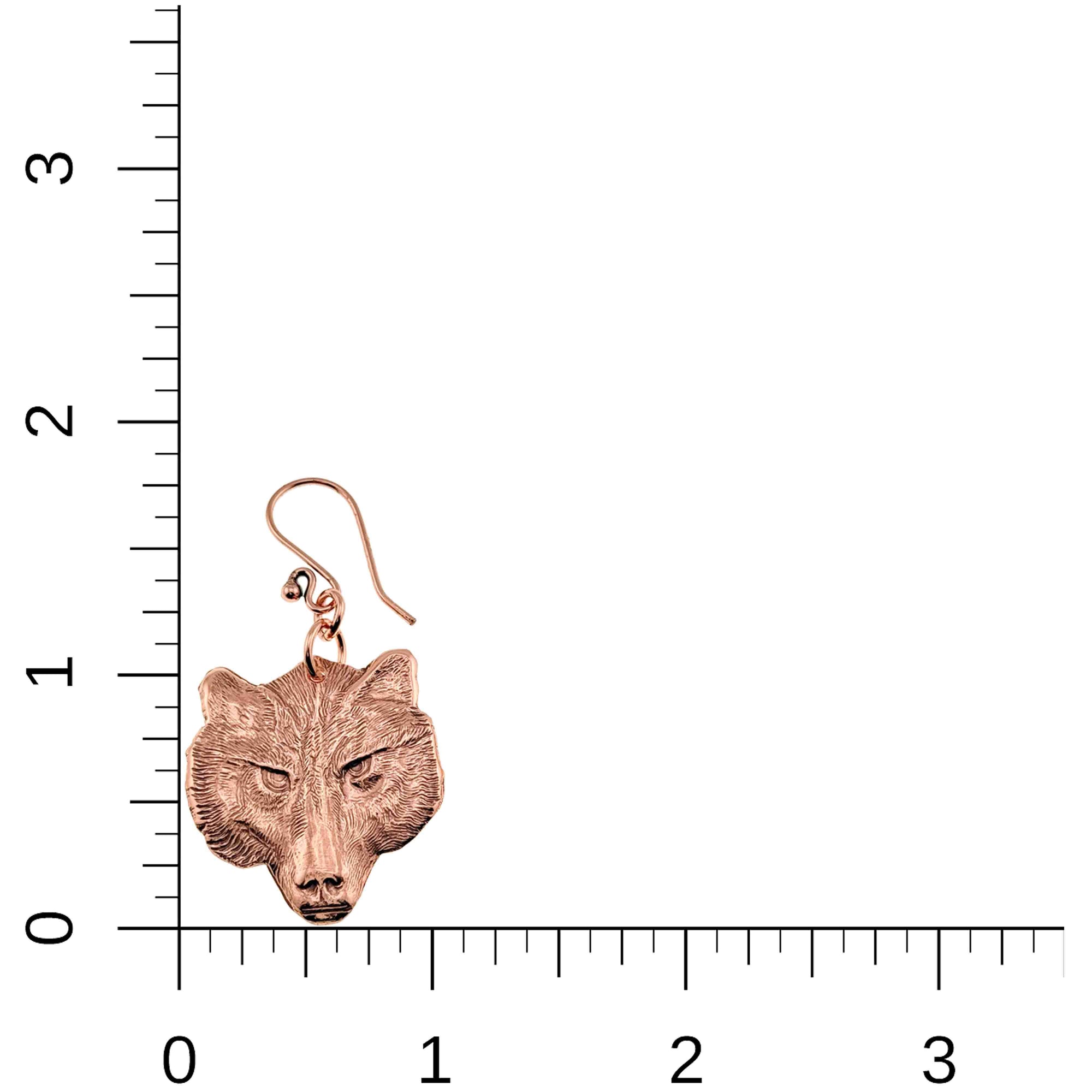 Copper wolf head earring on a ruler for scale