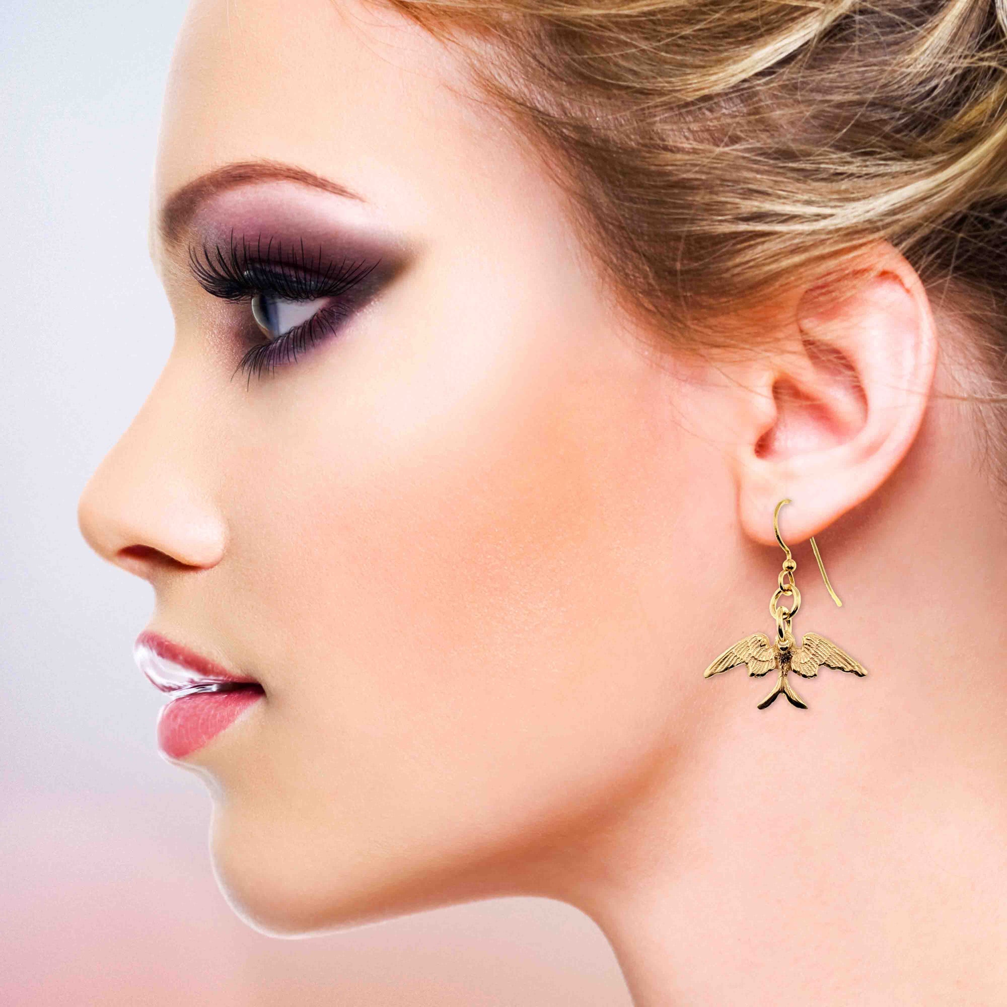 Close-up of a woman wearing Dainty Nu Gold Brass Swallow Earrings with a blurred background