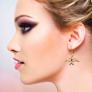 4 of 7: Close-up of a woman wearing Dainty Nu Gold Brass Swallow Earrings with a blurred background