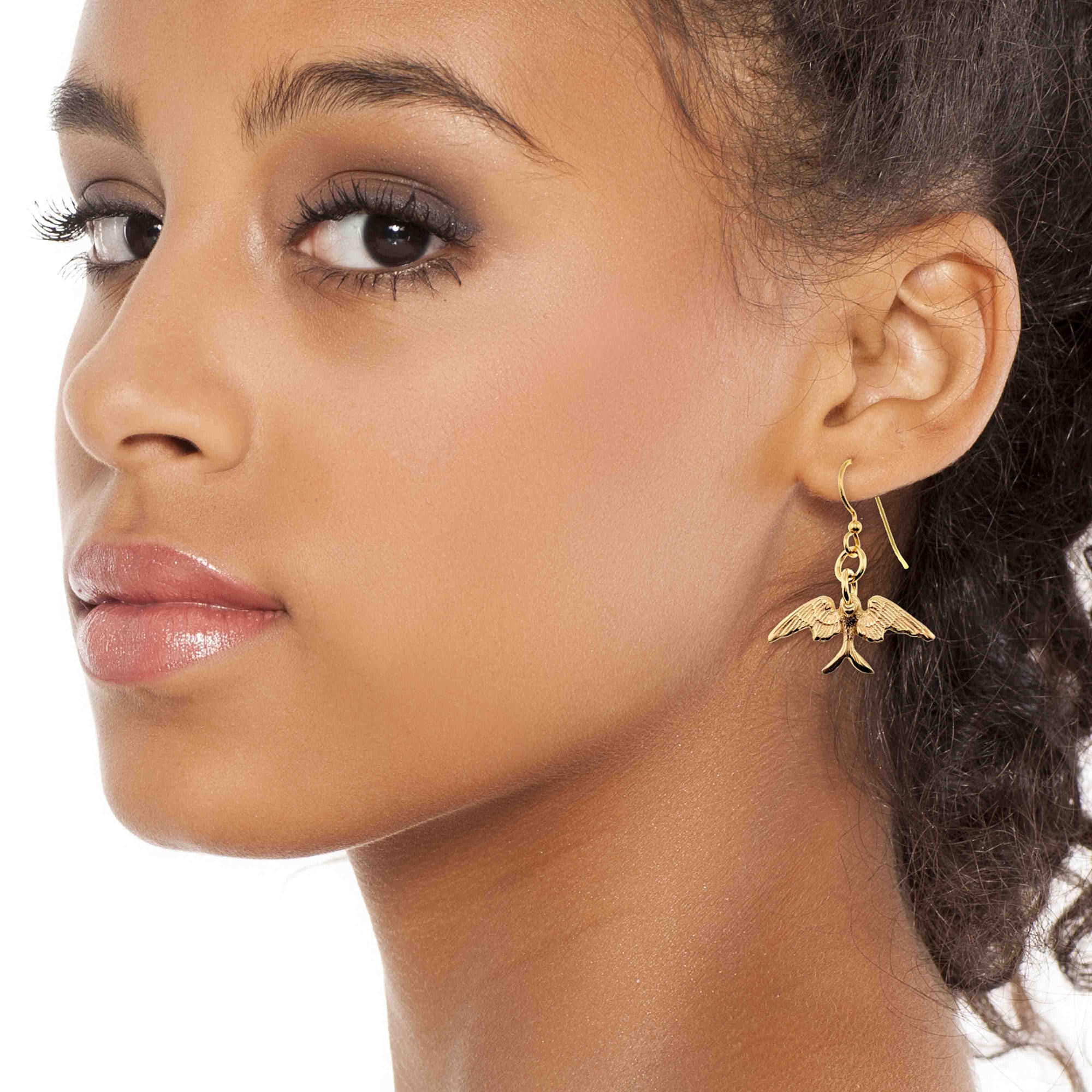 Close-up of a woman wearing Dainty Nu Gold Brass Swallow Earrings on a white background
