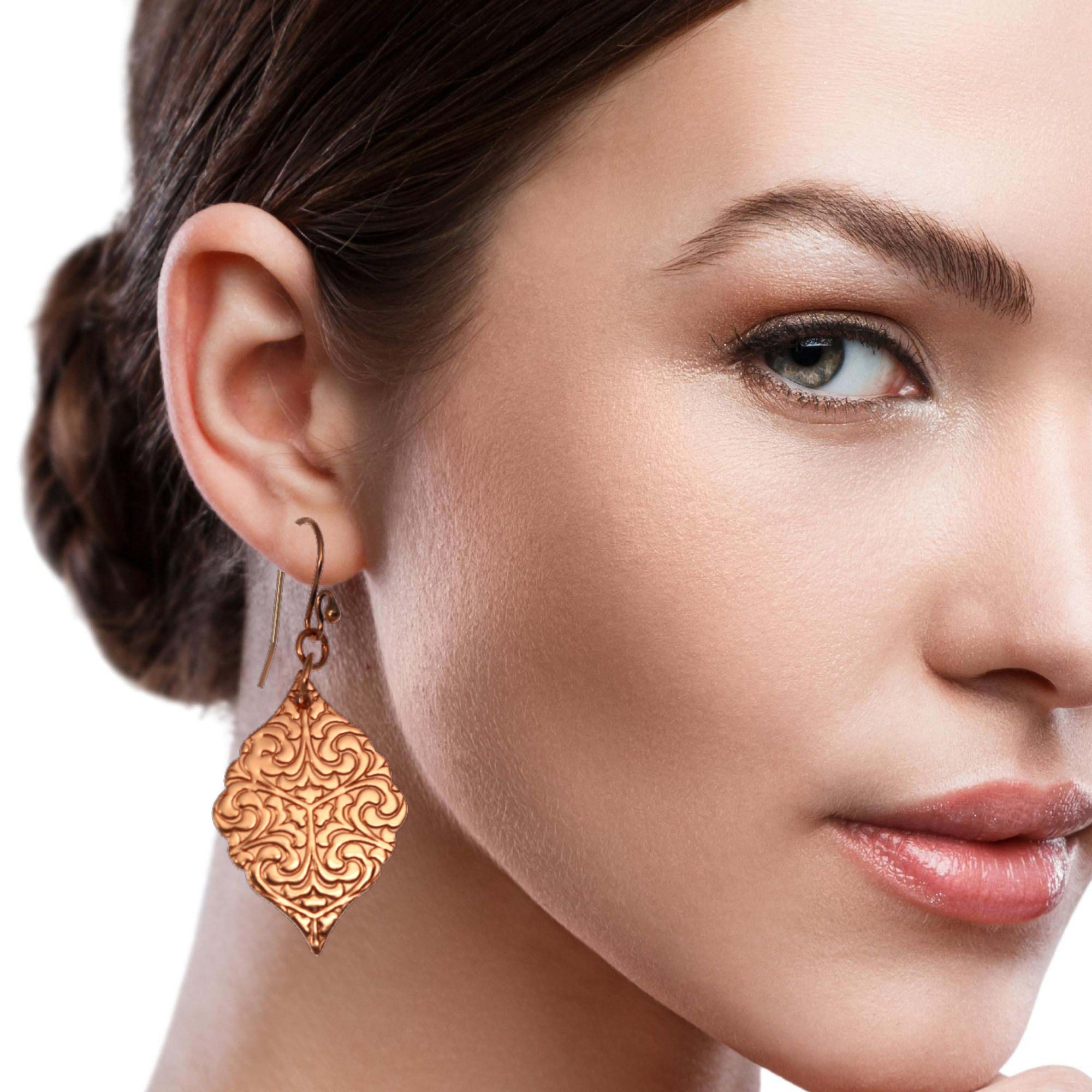 A woman wearing Damask Embossed Copper Moroccan Drop Earrings, adding elegance to her overall appearance.