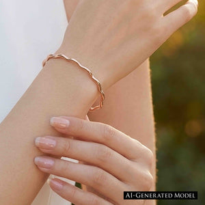 2 of 9: Close up of a woman’s wrist wearing a slim polished copper cuff bracelet with softly wavy, scalloped edges. The open bracelet wraps lightly around the wrist and reflects warm natural light. Her other hand rests gently below, showing pale pink manicured nails, while a softly blurred outdoor background gives the image a bright, elegant feel.  AI Generated Model.