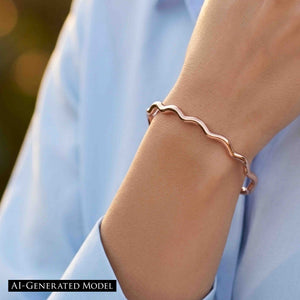 7 of 9: Close up of a wrist wearing a slim polished copper cuff bracelet with softly wavy, scalloped edges. The open cuff sits just above the wrist bone and has a smooth reflective finish that catches the light. The bracelet is styled with a light blue long sleeve top, with a softly blurred outdoor background that gives the image a warm natural feel.  AI Generated Model.