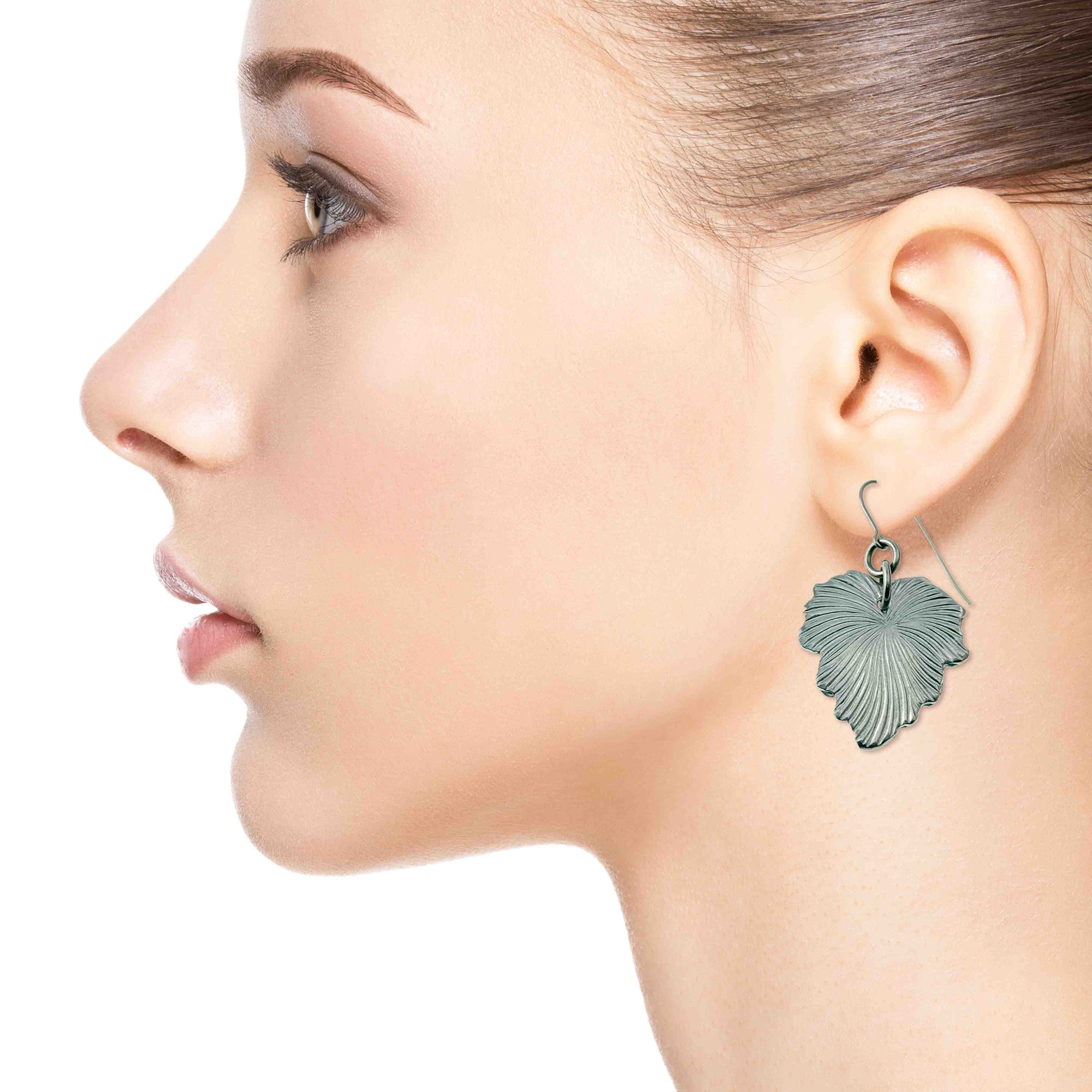 Close-up of a woman wearing Grape Leaf Aluminum Dangle Earrings on a white background