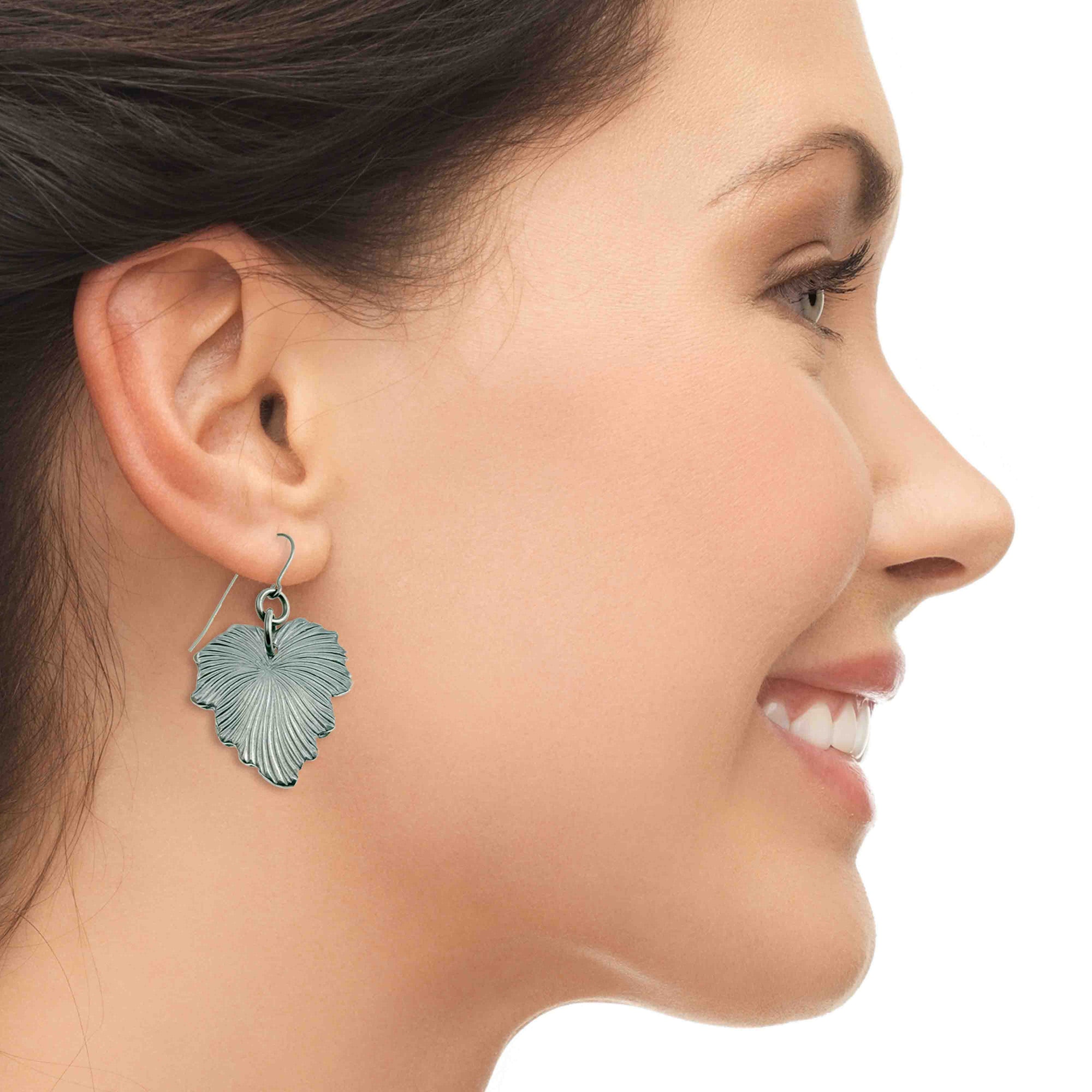 Close-up of a woman wearing a Grape Leaf Aluminum Dangle Earring on a white background