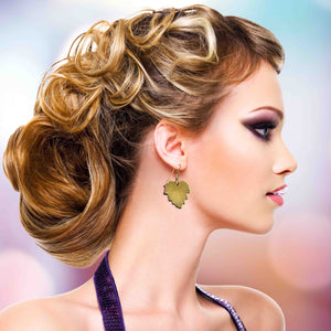 4 of 7: Woman with styled hair and Grape Leaf Nu Gold Brass Dangle Earrings against a blurred background