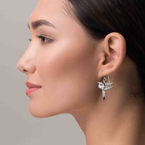 6 of 7: Close-up of a woman wearing a silver earring with a bird design on a neutral background