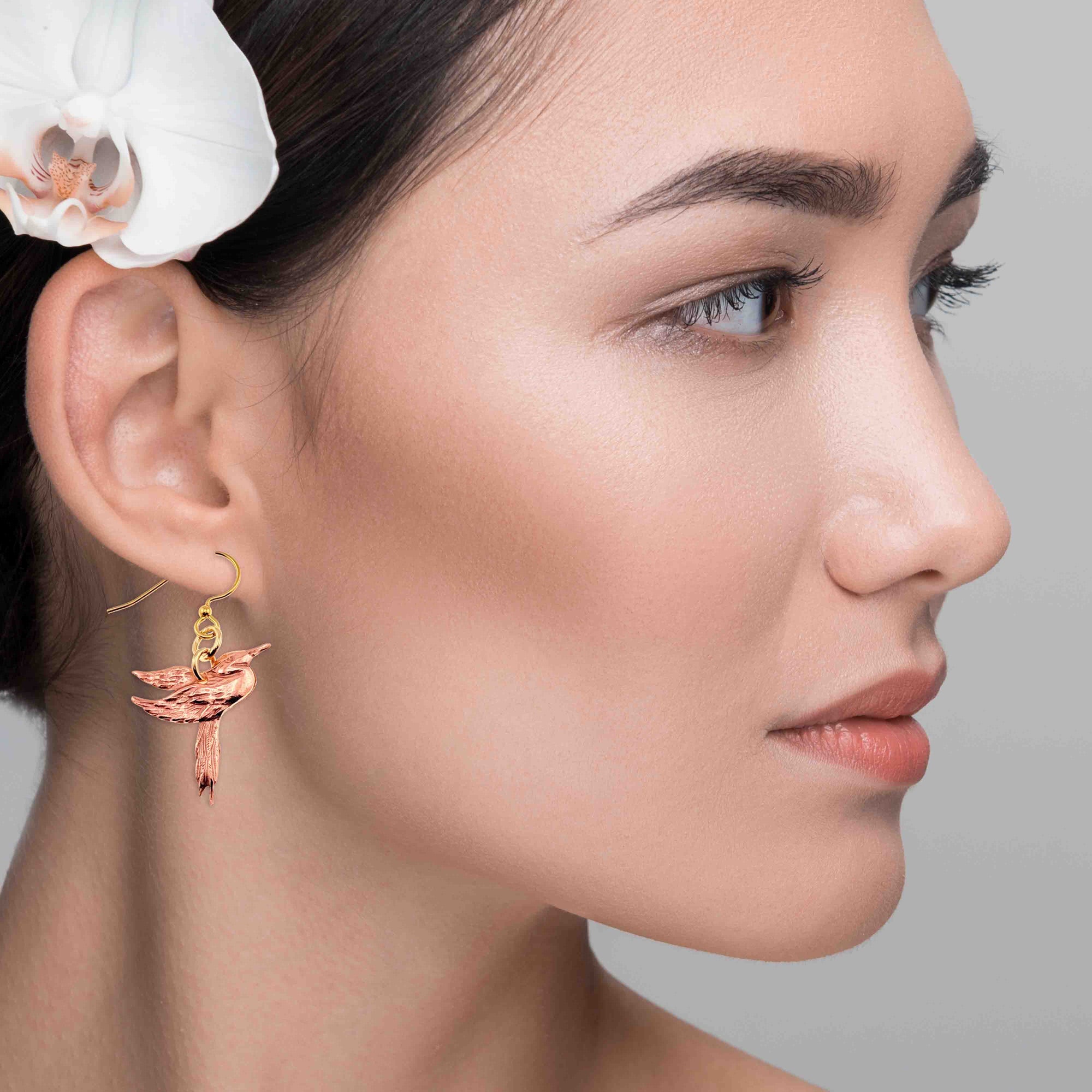 Close-up of a woman wearing a Great Blue Heron Copper Dangle Earring with an orchid flower in her hair.