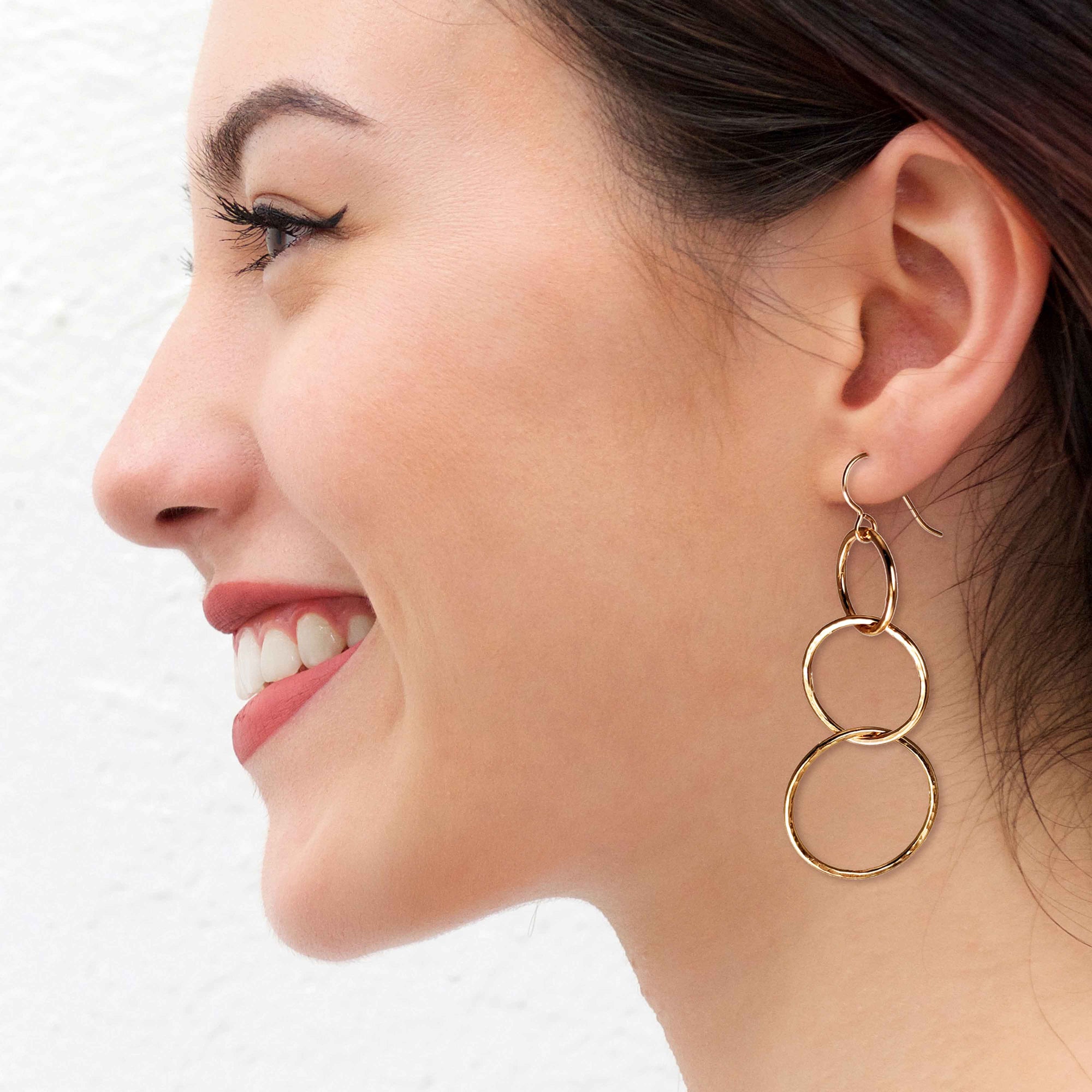 A Smiling Woman Wearing Hammered Bronze Three Tiered Dangle Earrings