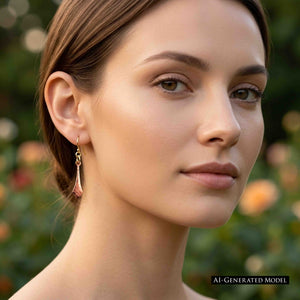 6 of 7: Woman with brown hair pulled back wearing a Hammered Copper Diamond Tip Drop Earring against a softly blurred garden background. The petite earring hangs freely beside her jaw and shows its slim shape, warm copper color, hammered texture, and pointed tip. Image includes an AI GENERATED MODEL label.