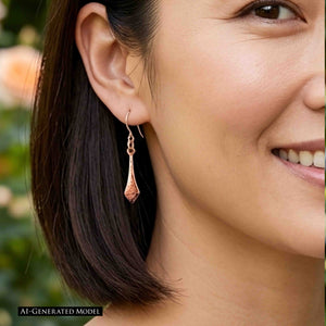 2 of 7: Close view of a smiling woman with dark straight hair wearing a Hammered Copper Diamond Tip Drop Earring outdoors. The narrow copper earring hangs beside her jawline, showing the pointed tip, hammered surface, and delicate ear wire. Image includes an AI GENERATED MODEL label.