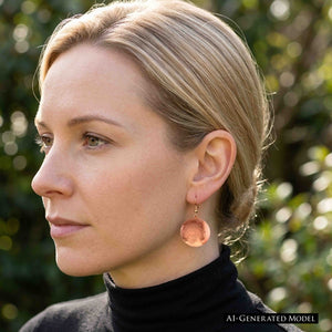 6 of 7: Woman with blonde hair pulled back wearing a Hammered Copper Disc Earring with a black turtleneck outdoors. The round polished copper disc hangs below the earlobe and shows how the 2 inch earring looks when worn. AI generated model image.