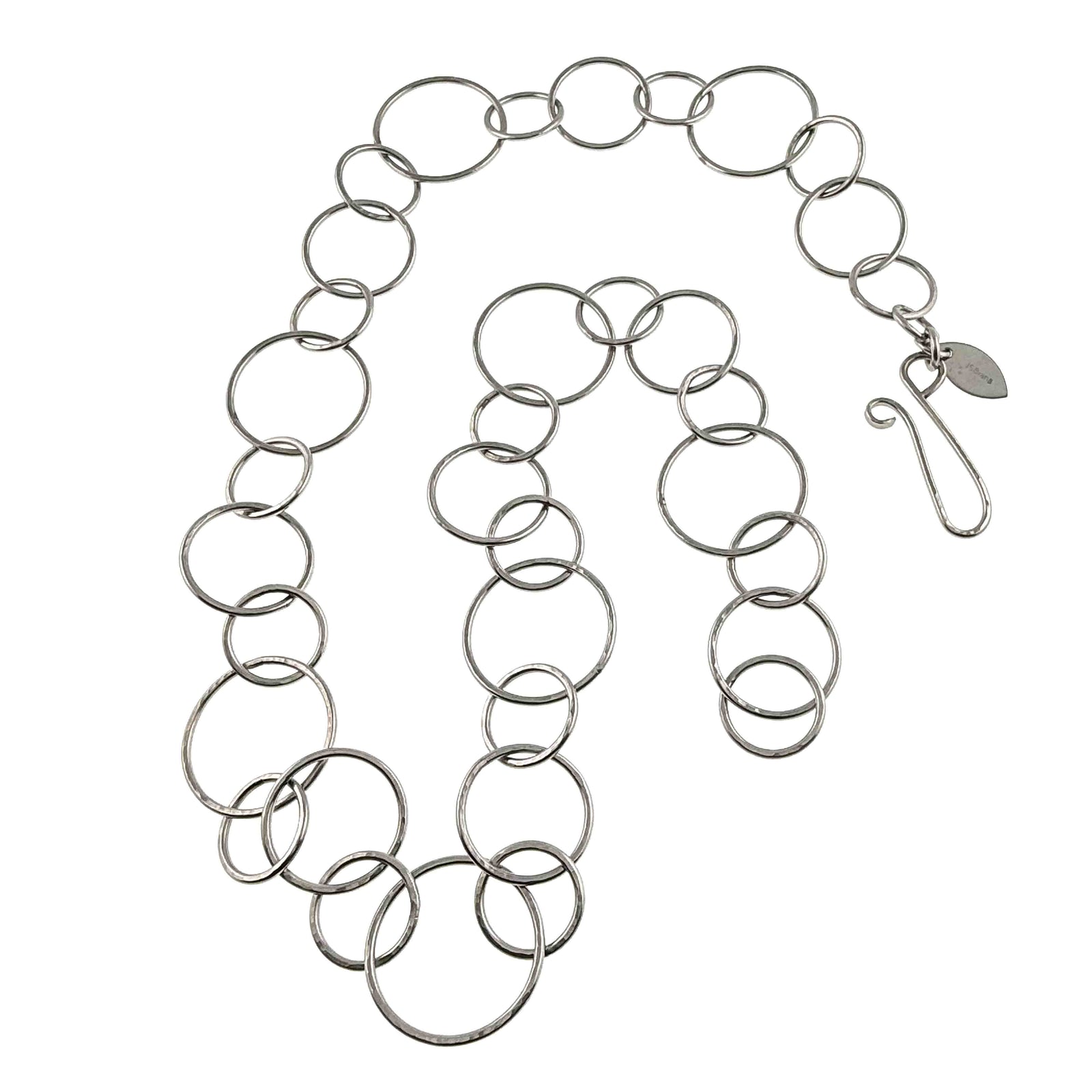 Full hammered stainless steel chain link necklace arranged on a white background with its handmade hook clasp and John S. Brana metal tag visible. The necklace features repeating round links in three sizes, with a polished silver tone finish and hammered texture.