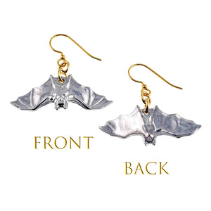 3 of 8: Front and back views of polished aluminum bat dangle earrings with gold tone French ear wires on a white background. The front shows raised gothic details across the wings, face, and body, while the back has a smoother molded surface. Gold text labels each view as FRONT and BACK.