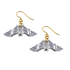 1 of 8: Pair of silver tone aluminum bat dangle earrings shown from the front on a white background. Each earring has spread wings, raised facial details, polished highlights, and a gold tone French ear wire joined by small gold rings.
