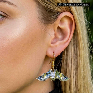 8 of 8: Close view of a blonde woman wearing a silver tone bat dangle earring with a gold tone French ear wire. The polished bat has spread wings and reflective details, with the ear and jewelry shown against blonde hair and a softly blurred green background.  AI Generated Model.