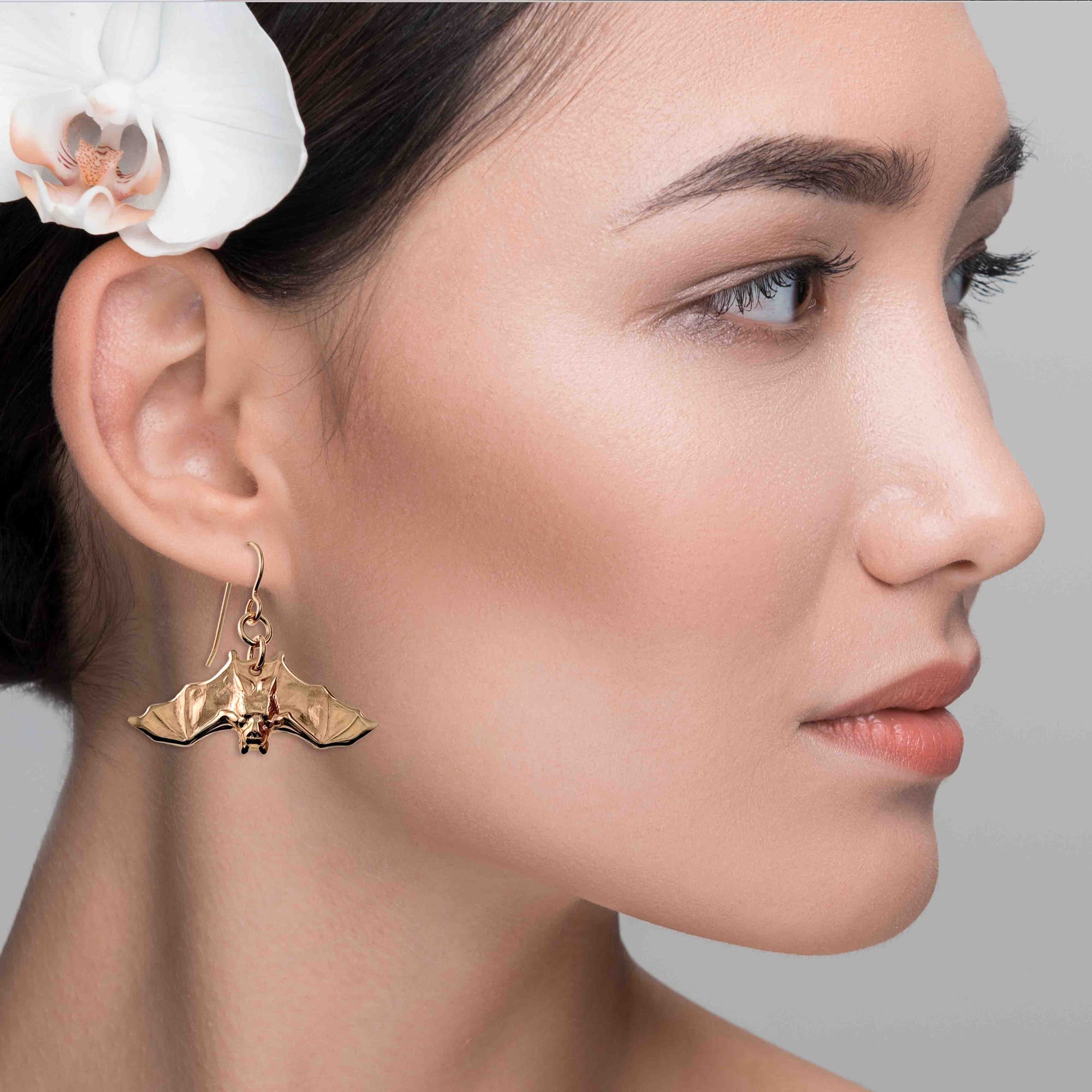 Close-up of a woman wearing a bronze earring with a bat design, against a neutral background.