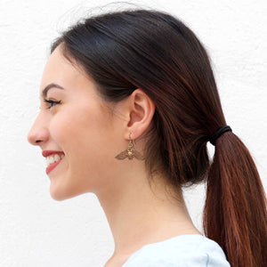 5 of 7: Woman in White T Shirt Wearing Hanging Bat Copper Dangle Earrings