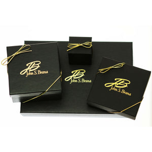 7 of 7: Luxury John S. Brana jewelry packaging displayed on a light background, featuring black textured gift boxes and a large matching gift box with gold foil logo. Each box is tied with a thin gold ribbon bow, creating an elegant presentation. The set includes multiple box sizes arranged together, highlighting the brand’s refined, gift ready packaging style.