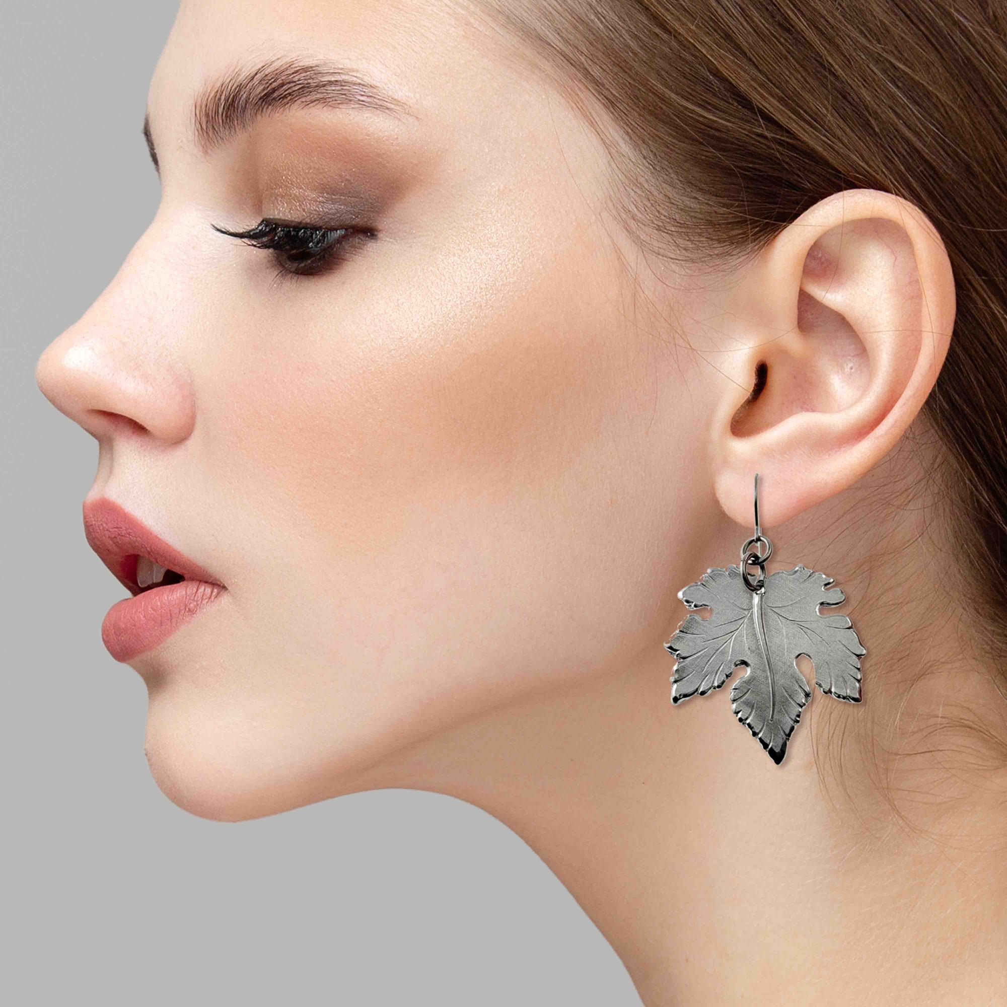 Close-up of a woman wearing a Large Maple Leaf Aluminum Dangle Earring against a gray background