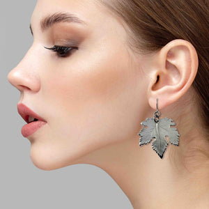 6 of 7: Close-up of a woman wearing a Large Maple Leaf Aluminum Dangle Earring against a gray background