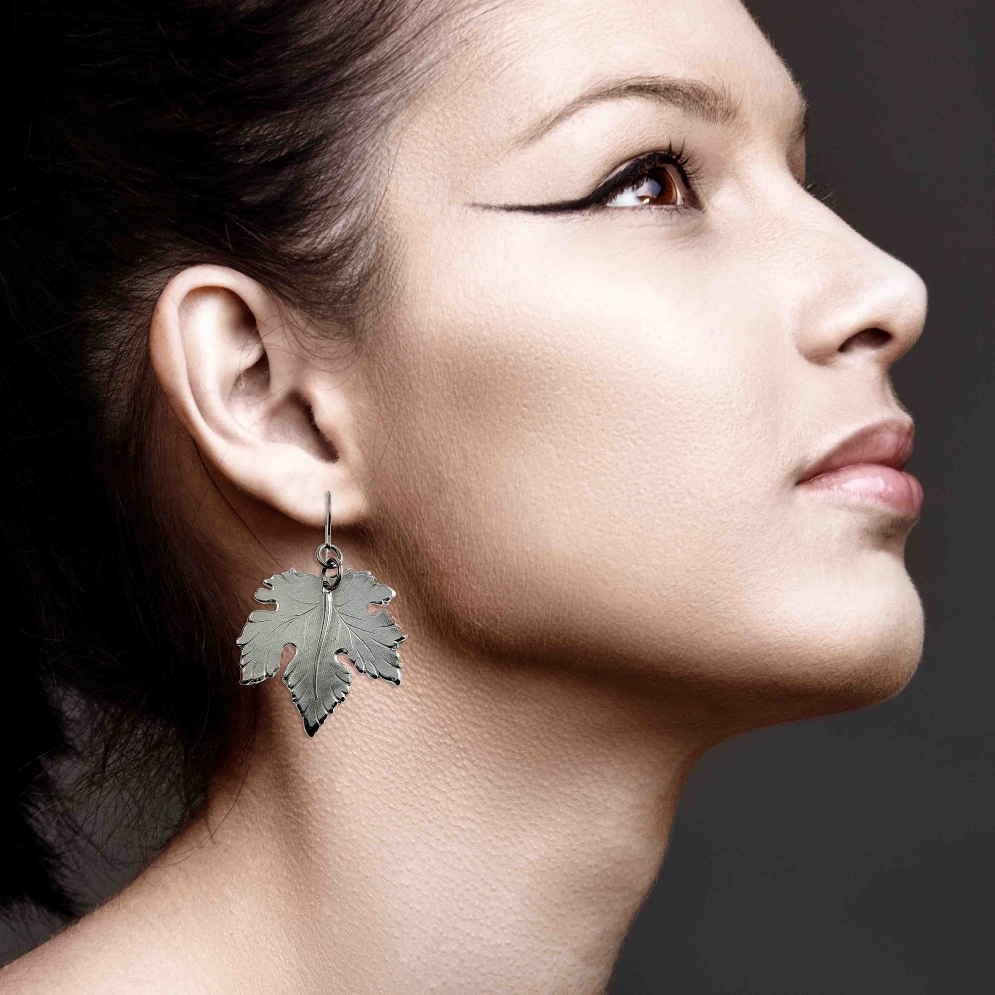 Close-up of a woman wearing Large Maple Leaf Aluminum Dangle Earrings against a dark background