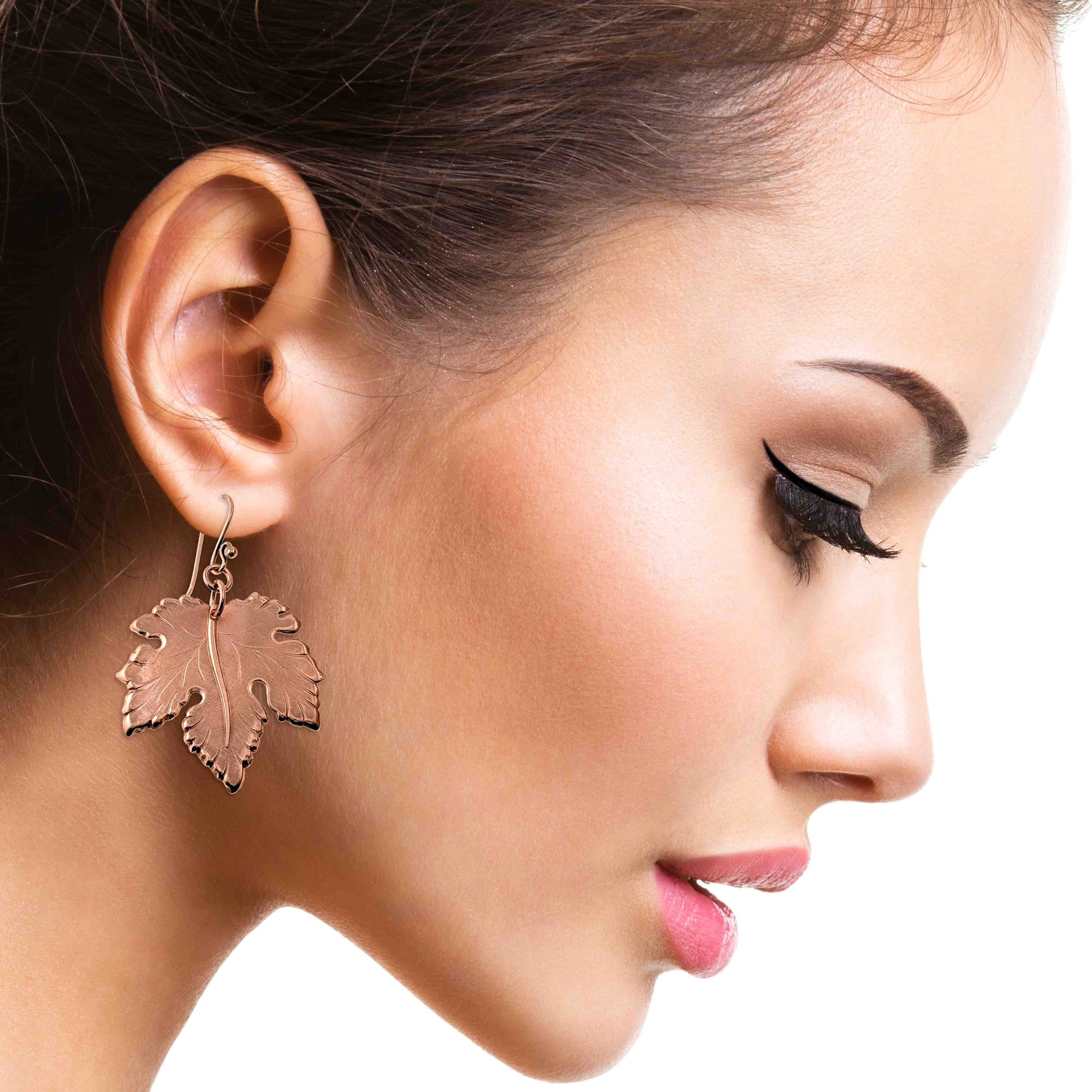 Close-up of a woman wearing Large Maple Leaf Copper Dangle Earrings  with a plain background