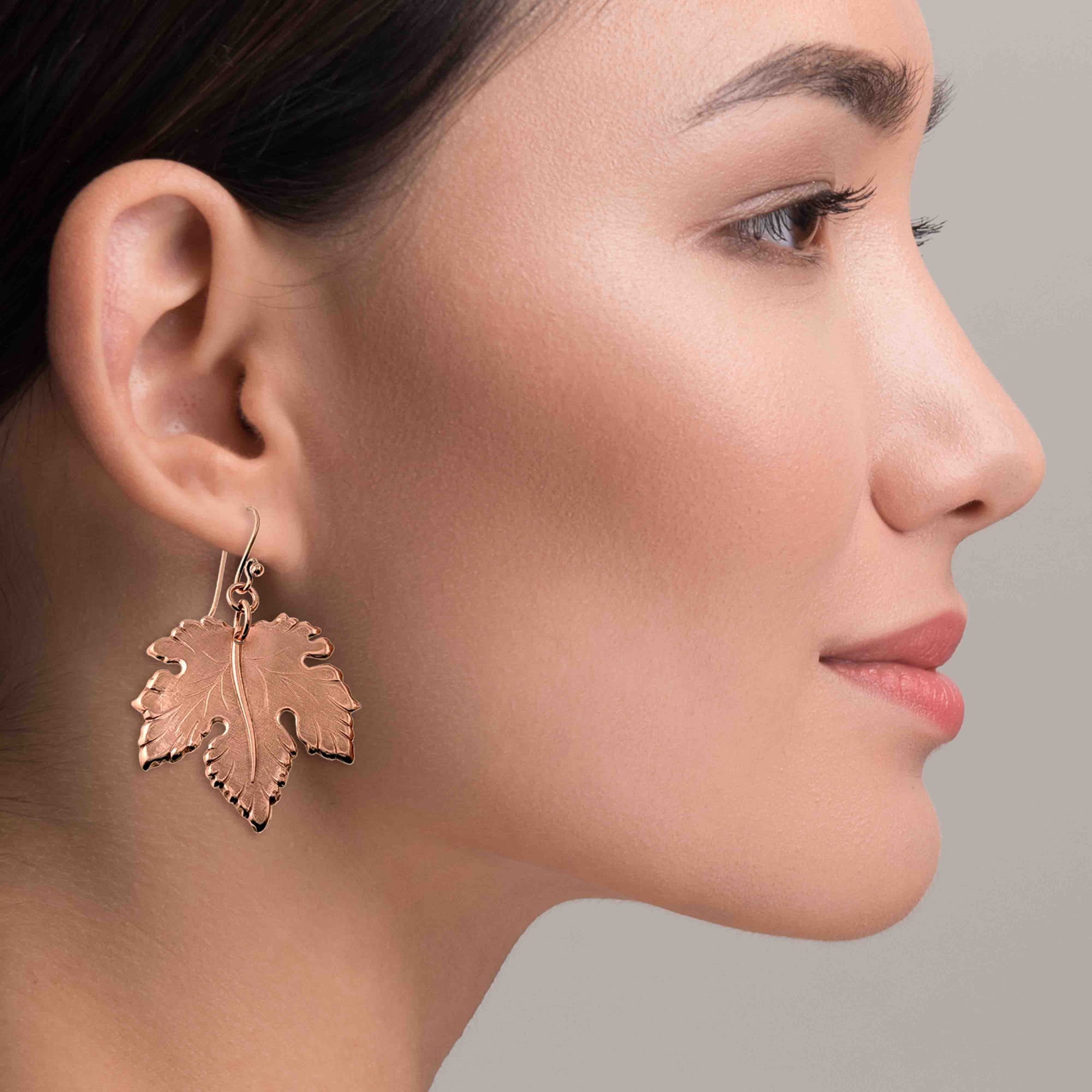 Close-up of a woman wearing Large Maple Leaf Copper Dangle Earrings  against a neutral background