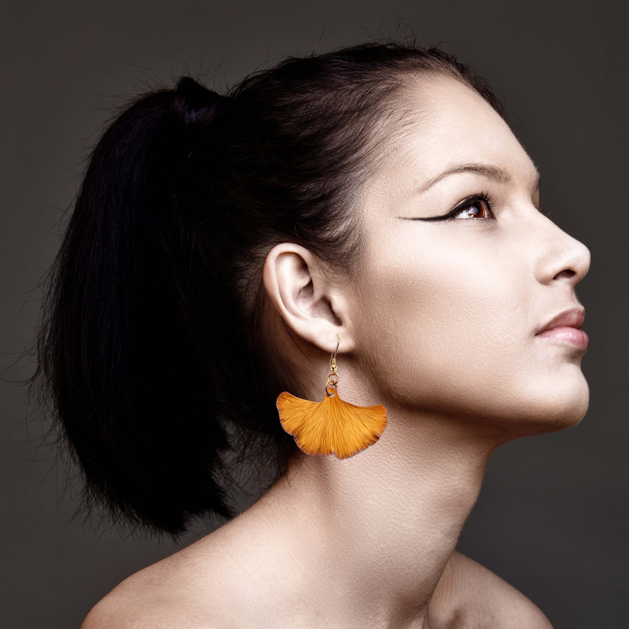 Elegant lady showcasing black hair and statement orange ginkgo leaf earrings