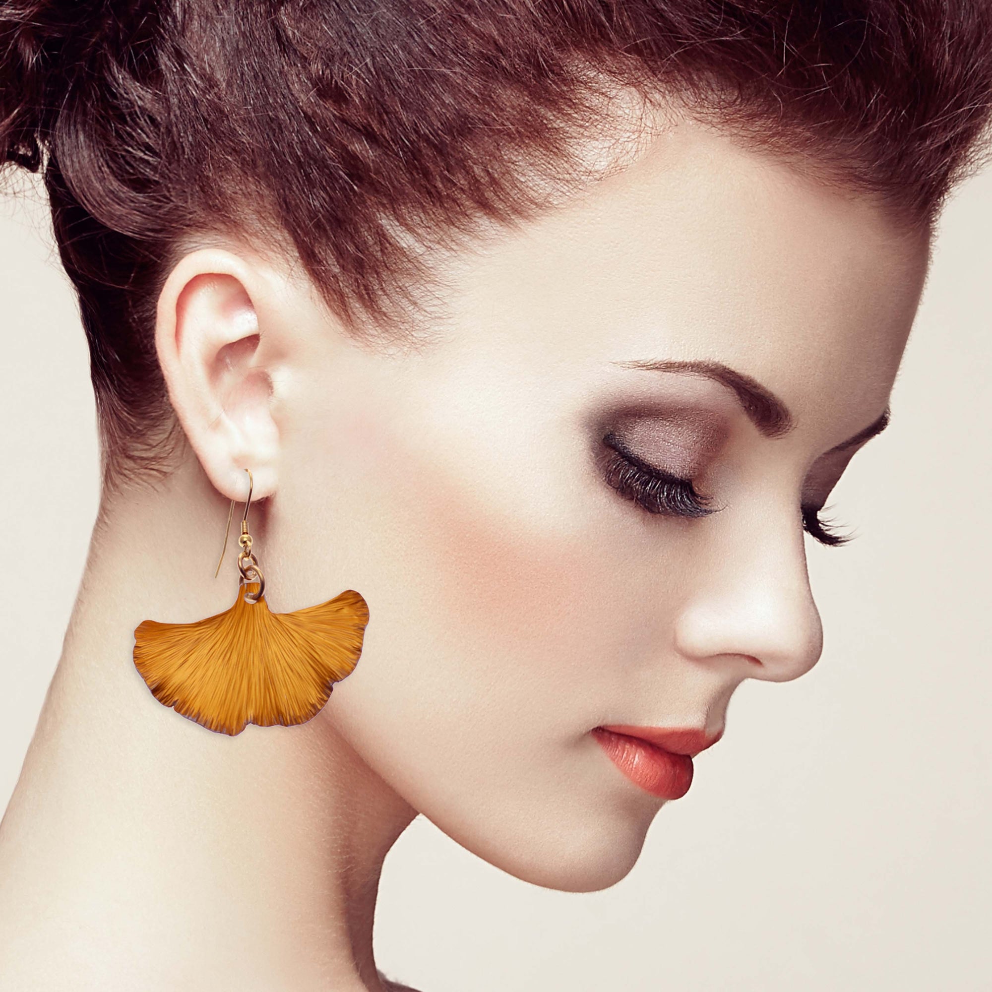 A woman wearing orange ginkgo leaf earrings, showcasing nature-inspired jewelry with elegance and style.