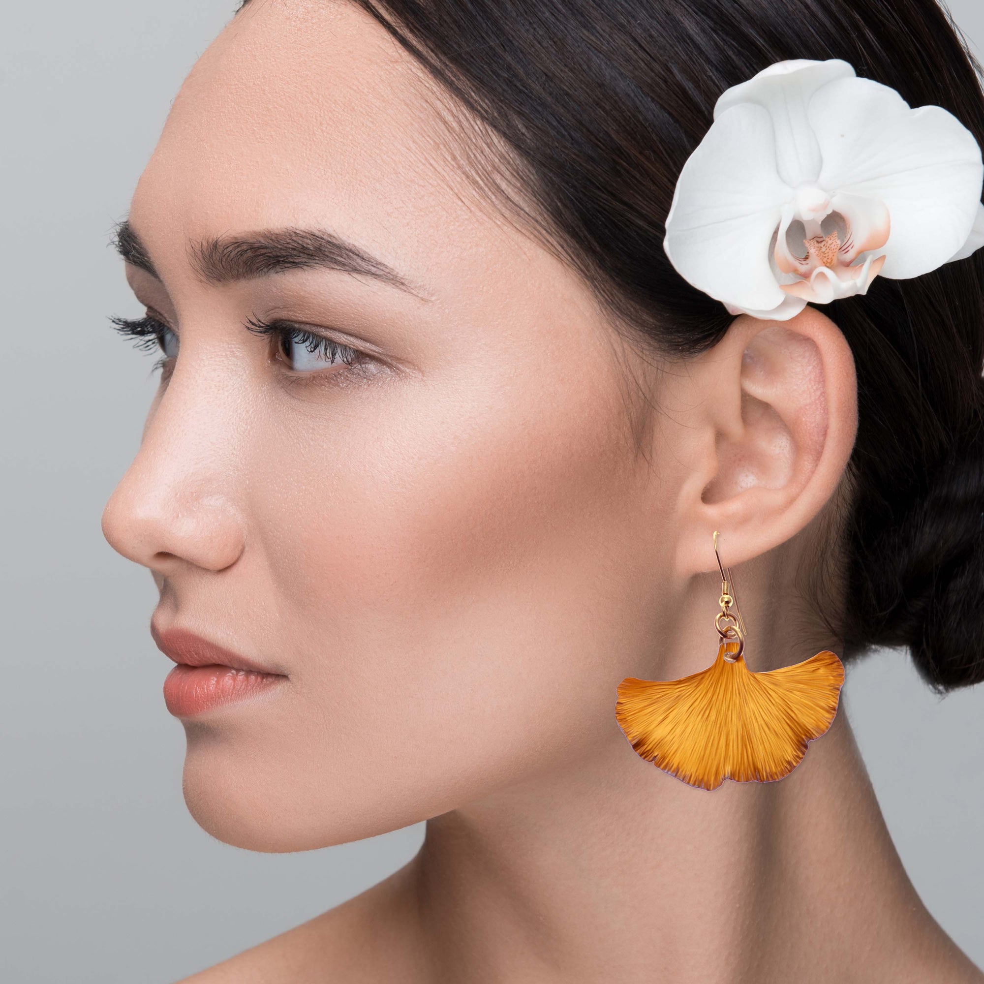 A woman with a flower in her hair and wearing an orange ginkgo leaf earring, radiating elegance and grace.