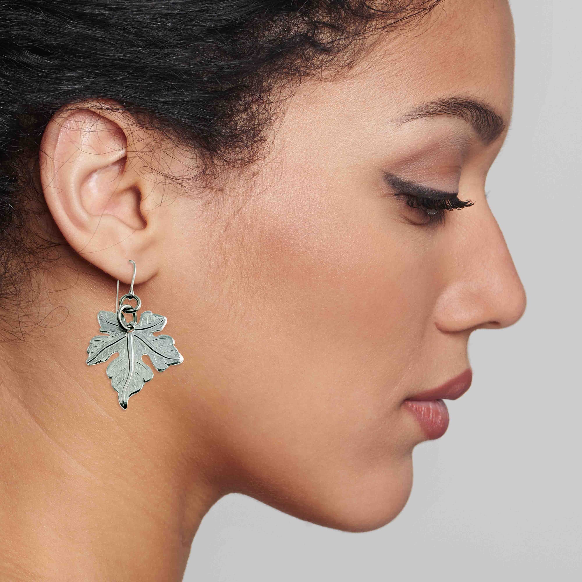Close-up of a woman wearing a Medium Maple Leaf Aluminum Dangle Earring against a neutral background